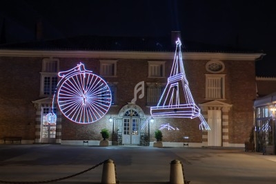 Façade d'un bâtiment en briques illuminée par des néons représentant un grand-bi et la tour Eiffel.