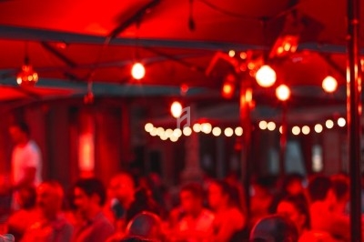 Terrasse animée d'un café en soirée, éclairée par des lumières rouges, avec des clients assis et discutant.