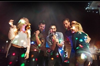 Des personnes chantent et dansent sous des lumières colorées dans une ambiance festive en intérieur.