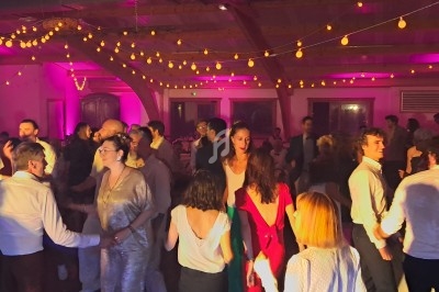 Des personnes dansent et discutent dans une salle éclairée par des guirlandes lumineuses et des lumières colorées.