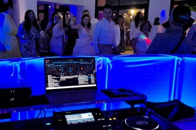 Vue depuis la table du DJ avec un ordinateur et une console, des invités dansent dans une ambiance lumineuse bleutée.