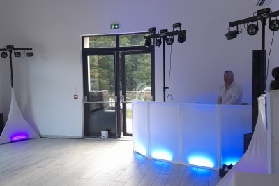Installation de matériel de sonorisation et d'éclairage dans une salle avec un DJ derrière une table lumineuse.
