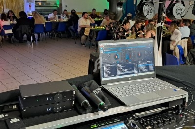 Vue d'une salle de réception avec des invités assis à des tables, un poste de DJ au premier plan.