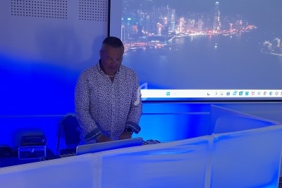 Homme debout devant un ordinateur, dans une salle éclairée en bleu, avec une projection de paysage urbain nocturne.