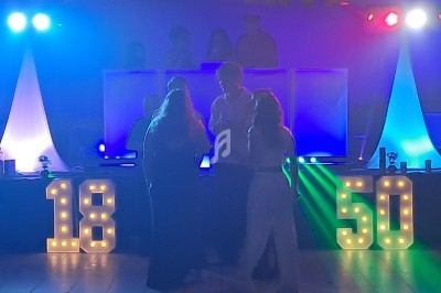 Personnes dansant devant une piste éclairée avec des chiffres lumineux ’18’ et ’50’ en arrière-plan.