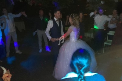 Un couple de mariés danse au centre d'une piste entourée d'invités sous des lumières colorées.