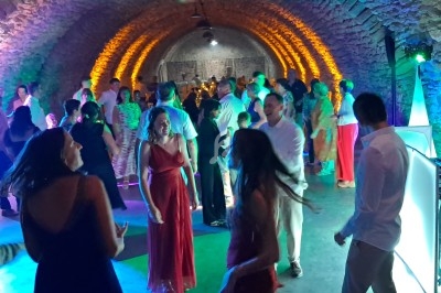 Personnes dansant et discutant dans une salle voûtée en pierre, éclairée par des lumières colorées.