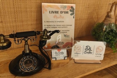 Téléphone rétro sur une table en bois utilisé pour un livre d'or audio, avec des instructions et des cartes de visite.