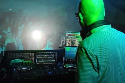 Un DJ de dos mixant sur une table de mixage dans une salle sombre éclairée par des projecteurs.