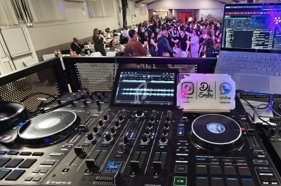 Vue depuis une table de mixage DJ avec une piste de danse animée et des invités en arrière-plan.