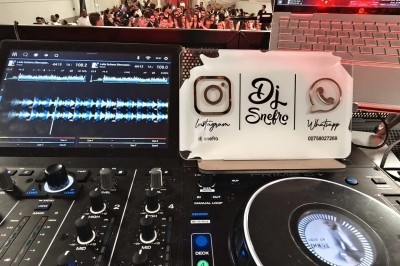 Vue rapprochée d'une table de mixage de DJ avec des écrans, des commandes et une plaque affichant des coordonnées.