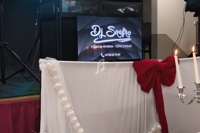 Un DJ mixe sur une scène éclairée, entourée de décorations de mariage avec bougies et tissu blanc.