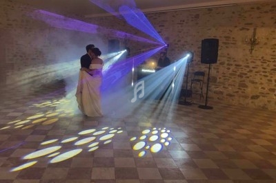 Un couple danse sous des jeux de lumière colorés dans une salle en pierre avec un DJ en arrière-plan.