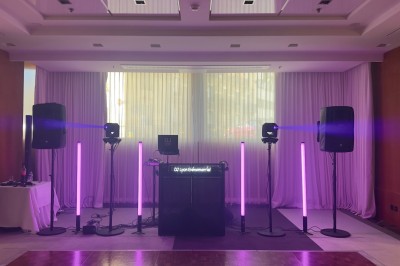 Installation de matériel de sonorisation et éclairage violet dans une salle avec rideaux blancs et parquet au sol.
