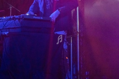 Un DJ mixe sur une table de mixage éclairée par des lumières violettes dans une ambiance de concert.