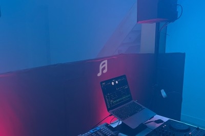 Équipement de DJ comprenant une table de mixage, des platines et un ordinateur, éclairé par des lumières colorées.