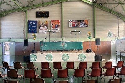 Salle de sport aménagée avec une scène décorée, des chaises alignées et des ballons pour un événement.