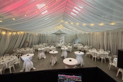 Salle de réception décorée avec des guirlandes lumineuses, des tables rondes nappées de blanc et des chaises en plastique.