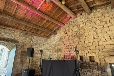 Salle en pierre avec un plafond en bois, décorée de ballons et lumières, abritant une table de DJ équipée.