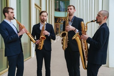 Quatuor de musiciens jouant du saxophone devant un bâtiment moderne avec des colonnes blanches.