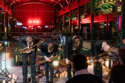 Quatre musiciens en costume s'inclinent avec leurs saxophones sur une scène éclairée, entourée de bougies.