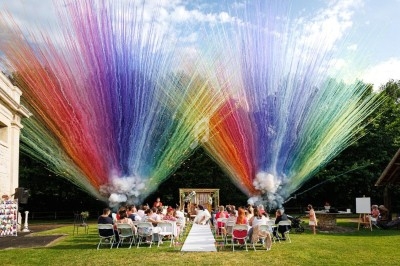 Des invités assis à une cérémonie en plein air, avec des explosions de fumée colorée en arrière-plan.