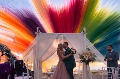 Un couple s'embrasse sous une arche décorée, avec un ciel vibrant de couleurs en arrière-plan.