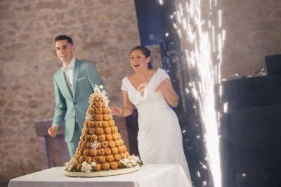 Un couple en tenue de mariage regarde une pièce montée éclairée par une fontaine de feu d'artifice en intérieur.