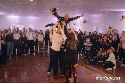 Un homme est porté en l'air par un groupe de personnes lors d'une fête, entouré d'invités et de confettis.