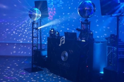 Salle de fête éclairée en bleu avec des projecteurs, deux boules à facettes et une table de DJ équipée.