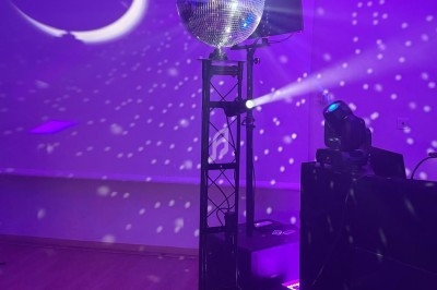 Boule disco éclairée projetant des reflets lumineux sur un mur, avec projecteurs et ambiance violette dans une salle.