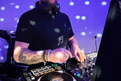 Un DJ mixe de la musique sur une console dans une ambiance lumineuse avec des reflets et des points lumineux.