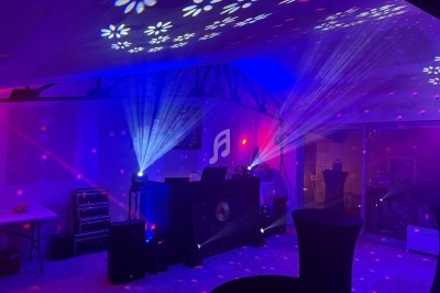 Salle de réception éclairée par des jeux de lumières colorés avec une table de mixage et des haut-parleurs.