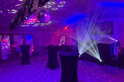 Salle de réception décorée avec des lumières colorées, une boule disco et des tables hautes noires.