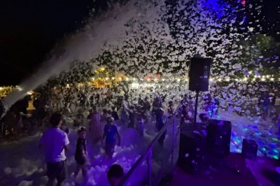 Des personnes participent à une fête nocturne avec des canons à mousse et des éclairages colorés.