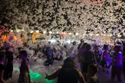 Des personnes participent à une fête de mousse en plein air, entourées de lumière et d'une ambiance nocturne festive.