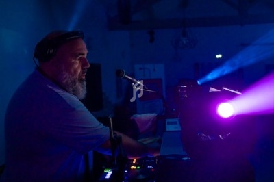 Un DJ mixe de la musique dans une ambiance sombre, éclairé par des lumières violettes et bleues.