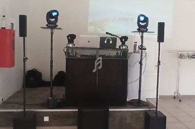 Installation de matériel de sonorisation et d'éclairage sur une petite scène dans une salle intérieure.