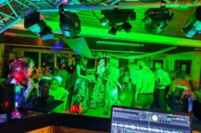 Vue depuis une cabine de DJ sur une piste de danse éclairée par des lumières colorées, avec des invités en mouvement.