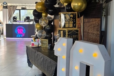 Décoration de fête d'anniversaire avec ballons noirs et dorés, table ornée et chiffre lumineux ’18’ au premier plan.