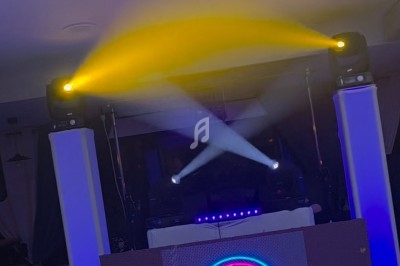 Pupitre de DJ éclairé par des projecteurs jaunes et blancs, avec un logo lumineux ’DJ's & Co’ au centre.