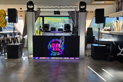 Configuration d'une piste de danse avec équipement DJ, écran lumineux, enceintes et décorations dans un espace lumineux.