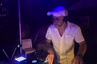 Un DJ portant une chemise blanche et une casquette mixe de la musique sur une console dans un environnement sombre.