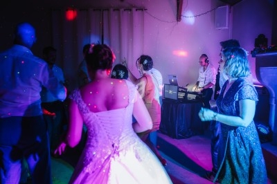 Des personnes dansent sous des lumières colorées lors d'une fête, avec un DJ en arrière-plan.