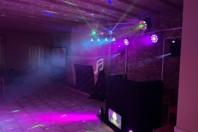 Jeu de lumières colorées et fumée dans une salle avec un plafond en bois et des murs en pierre.