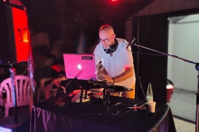 Un DJ mixe de la musique sur une table équipée d'un ordinateur portable et de matériel audio lors d'un événement en soirée.