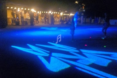 Jeu de lumières bleues projetées au sol lors d'un événement nocturne en extérieur, avec des silhouettes en arrière-plan.