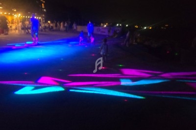 Des projections lumineuses colorées illuminent une promenade nocturne avec des silhouettes de personnes en arrière-plan.