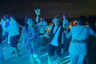 Des personnes dansent pieds nus sur une piste éclairée de lumières colorées, en extérieur et de nuit.