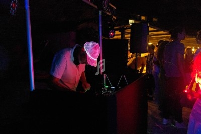 Un DJ mixant de la musique dans une ambiance nocturne avec des lumières colorées et des personnes dansant autour.